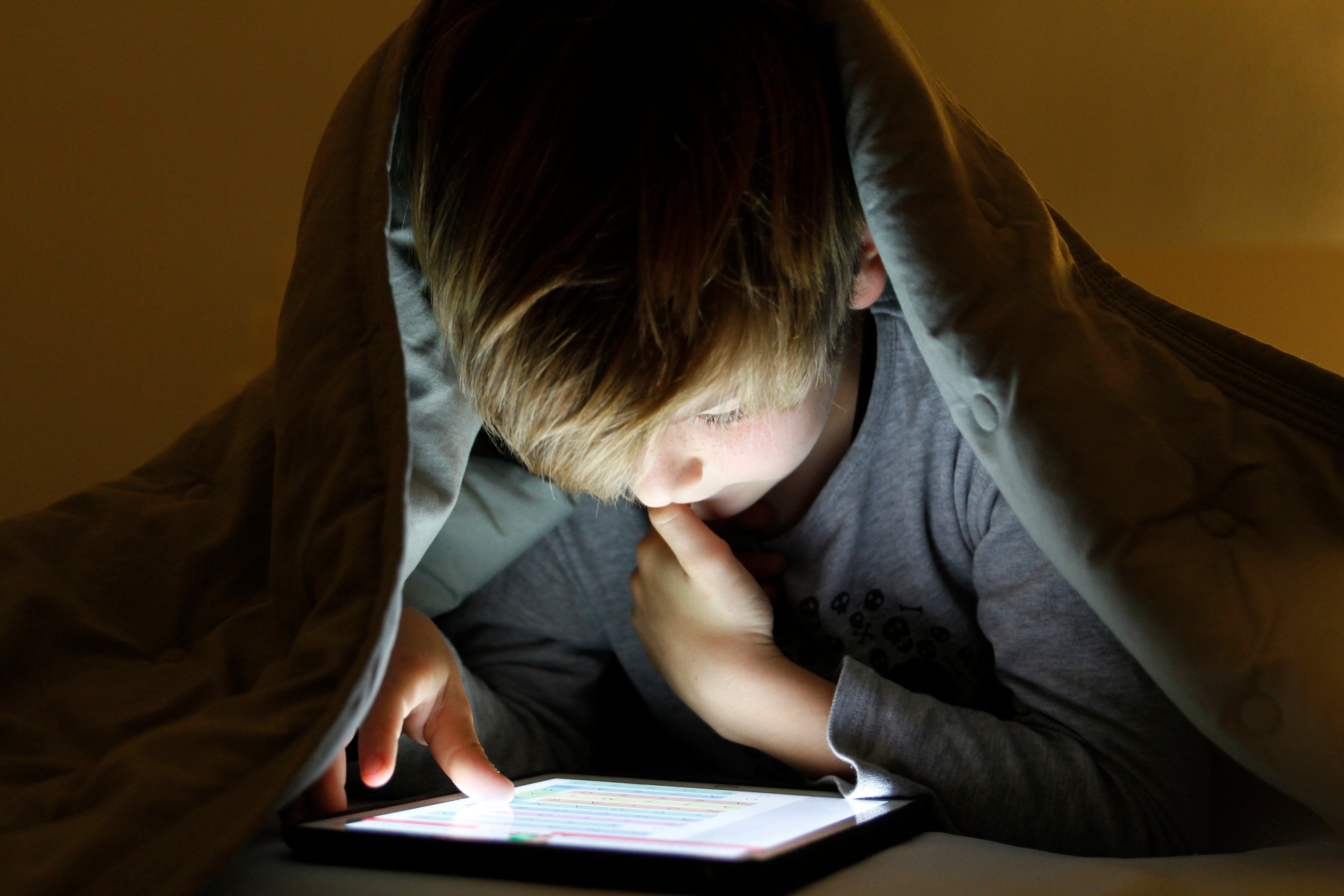 Boy using digital tablet under bed covers at night