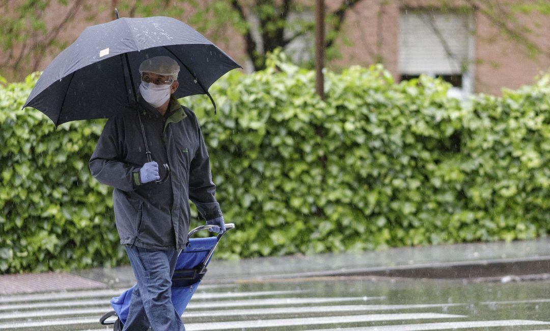 Un hombre protegido con mascarilla y paraguas tras las lluvias. 