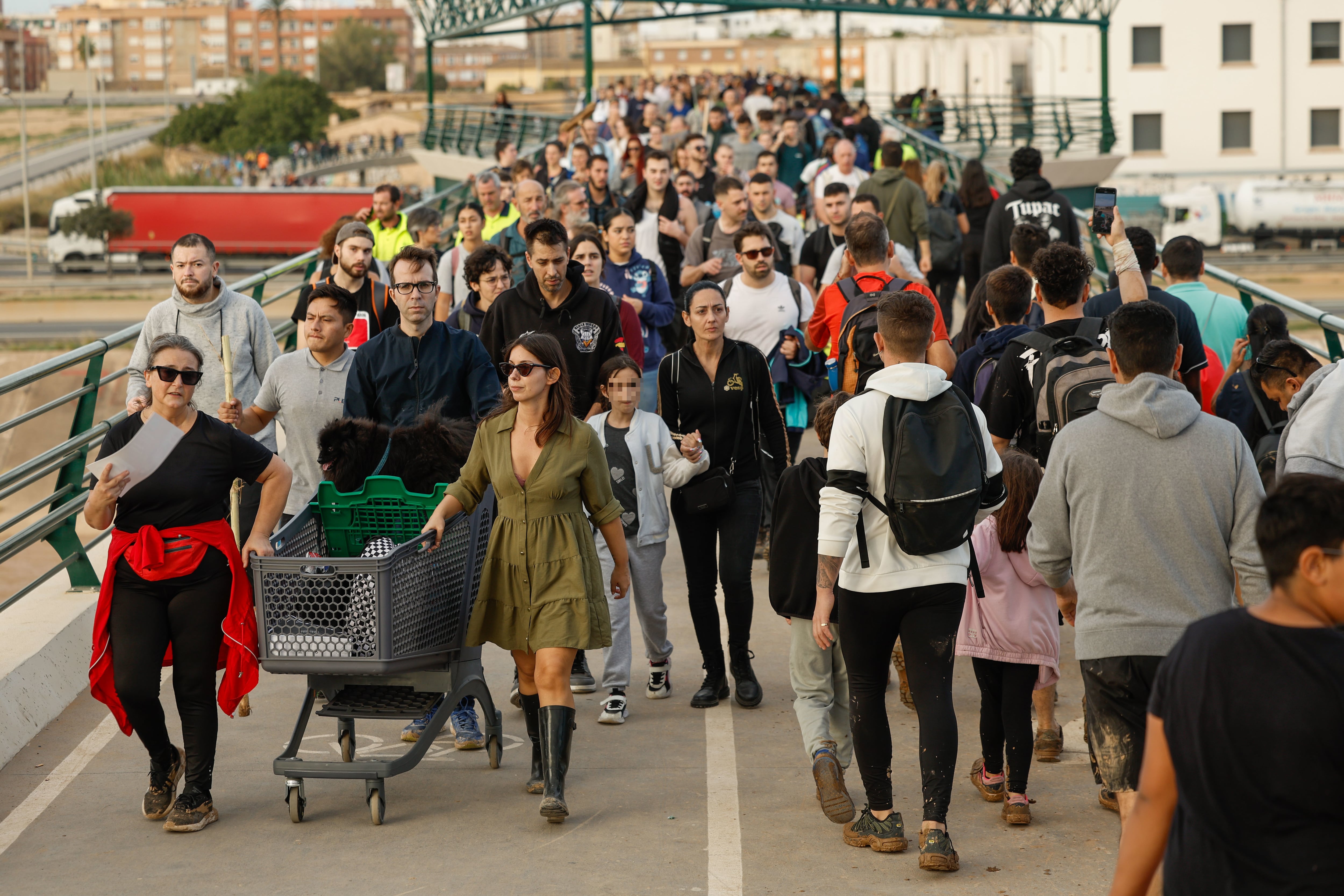 Cientos de personas cruzan la pasarela de Valencia hacia el barrio valenciano de La Torre, con alimentos y herramientas para ayudar al desescombro tras DANA, este jueves.