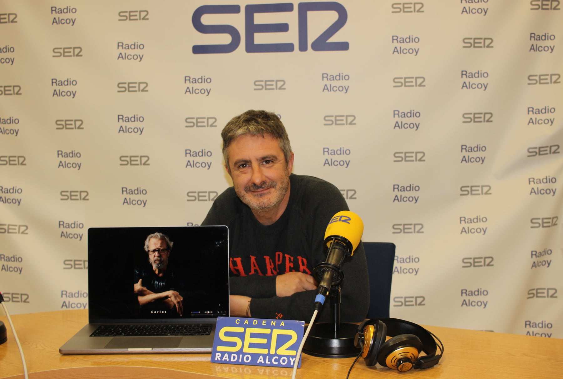 Toni Miranda en l'estudi central de Radio Alcoy amb una de les imatges de l'exposició a l'aire lliure, en concret la del pintor que fa poc ens va deixar Carlos Merchán