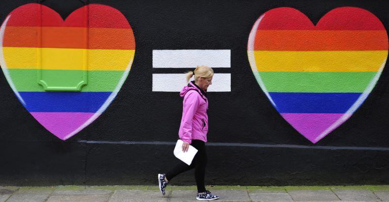 Una mujer camina junto a una pintada de dos corazones con los colores del arcoíris en Dublín, Irlanda.