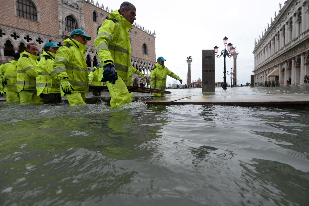 Operarios instalan pasarelas de madera para poder pasar sobre el agua que vuelve a inundar Venecia.