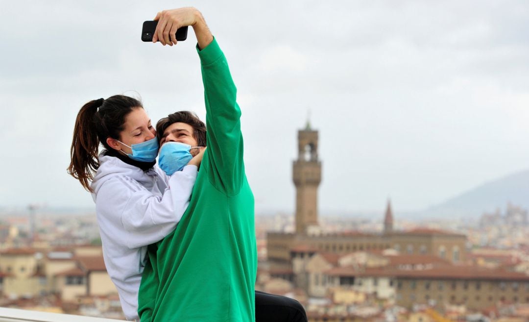 Una pareja con mascarillas se hacen una foto en el Piazzale Michelangelo de Florencia