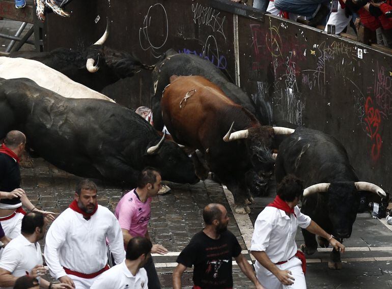 La manada de toros de la ganadería gaditana Núñez del Cuvillo toma en tropel la curva de entrada a la calle Estafeta con el pavimento mojado por la lluvia reciente