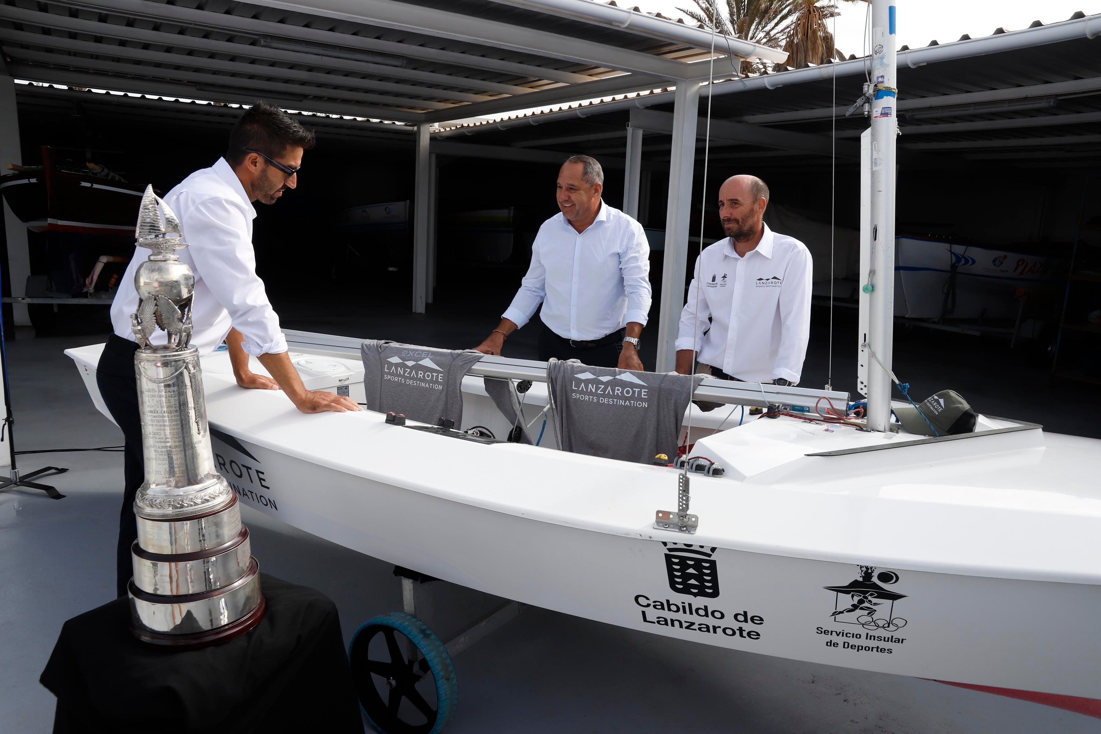 El consejero de Deportes del Cabildo de Lanzarote, Juan Monzón, junto a los dos regatistas Alfredo González y Cristian Sánchez y la embarcación que les ha cedido para el Mundial de Snipe.