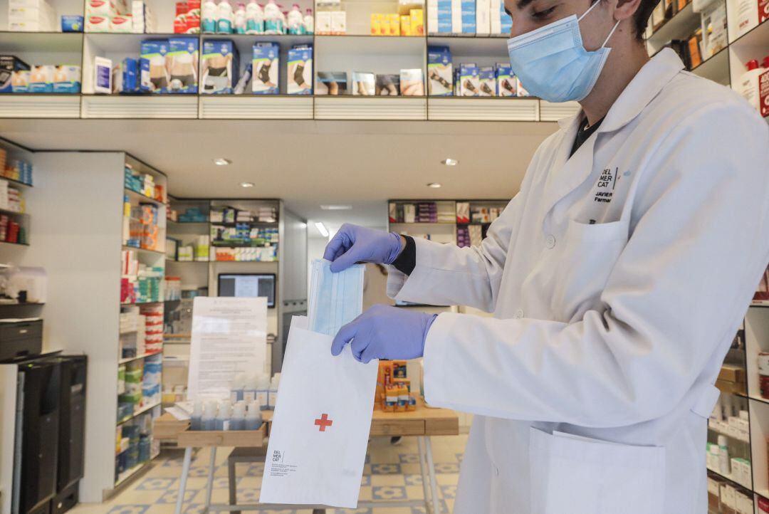 Un farmacéutico da una mascarilla durante el reparto de mascarillas gratuitas contra el Covid19 a mayores de 65 años y colectivos de riesgo que ayer arrancó en la Comunitat Valenciana. Después de algunas colas a primera hora en determinadas poblaciones, la distribución se ha llevado a cabo con normalidad, en Valencia