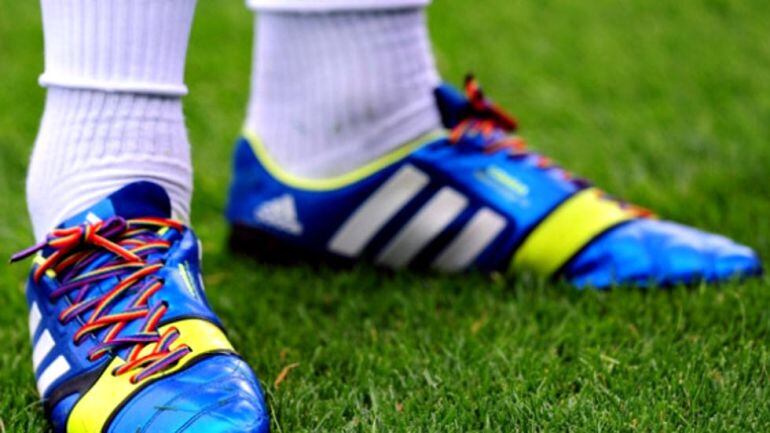 Un futbolista lleva atadas las botas con cordones con los colores del arcoiris 