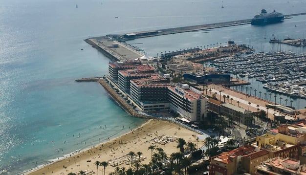 Imagen del Postiguet y del puerto de Alicante con el edificio del Hotel Meliá en el centro.