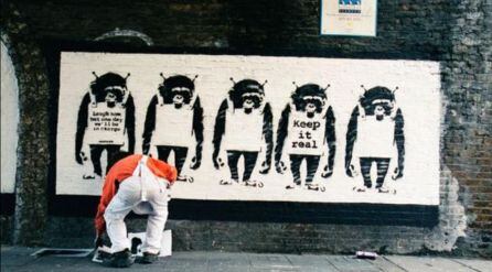 Banksy de espaldas mientras pinta uno de sus murales