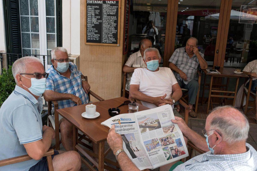 Varias personas con mascarillas sentadas en la terraza de un bar.