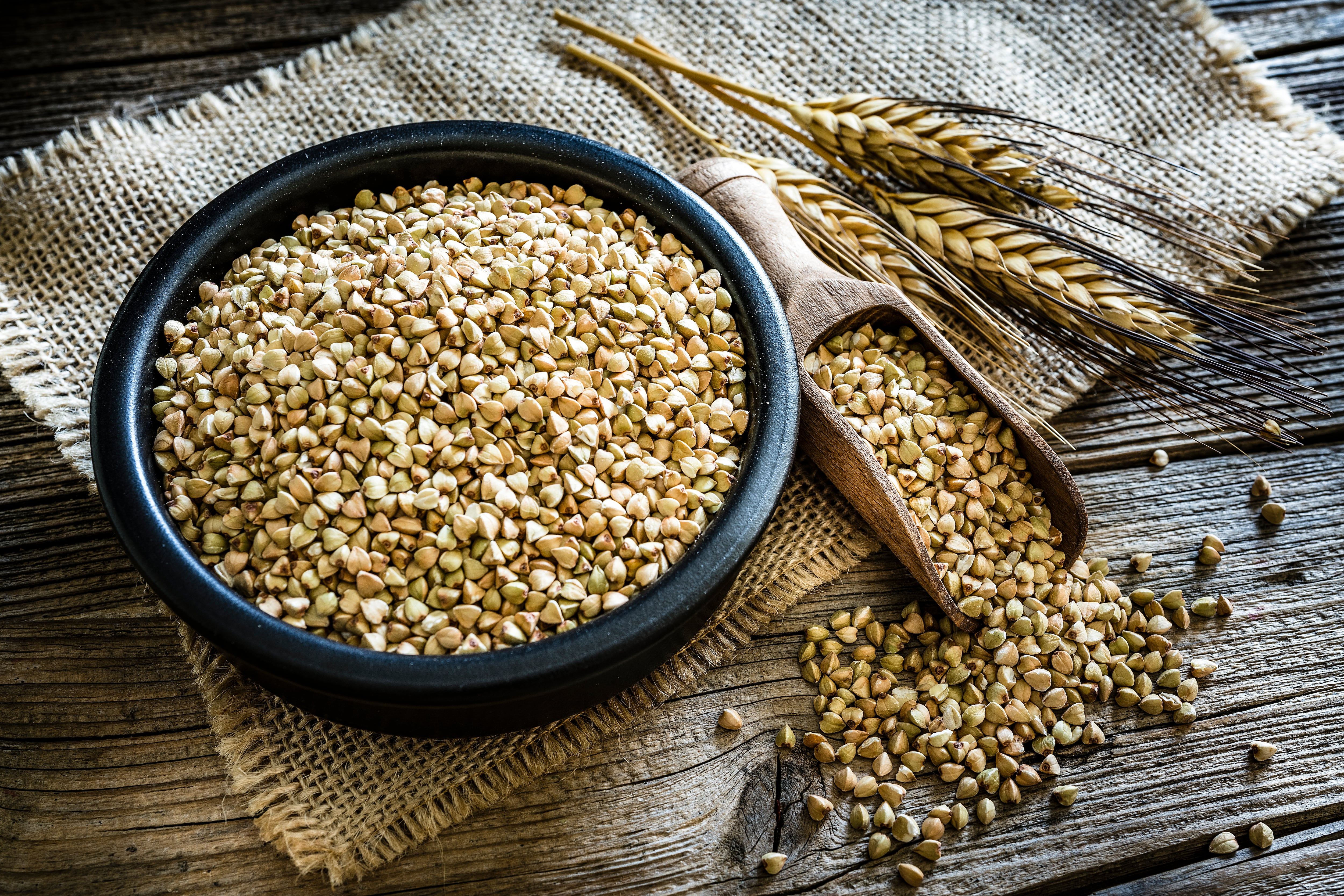 Dietary fiber: high angle view of wholegrain buckwheat in a black bowl on rustic wooden table. A wooden serving scoop with buckwheat is beside the bowl. Predominant color is brown. XXXL 42Mp studio photo taken with SONY A7rII and Zeiss Batis 40mm F2.0 CF