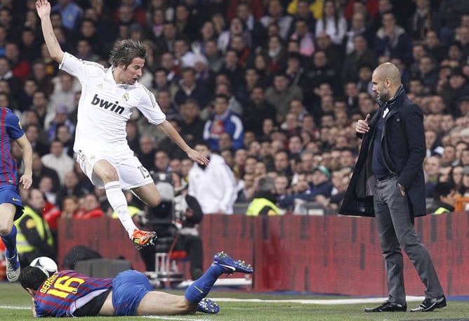 El defensa portugués del Real Madrid, Coentrao, salta por encima del centrocampista del F. C. Barcelona, Sergi Busquets, ante el entrenador blaugrana, Pep Guardiola, durante el encuentro correspondiente a la ida de los cuartos de final de la Copa del Rey,