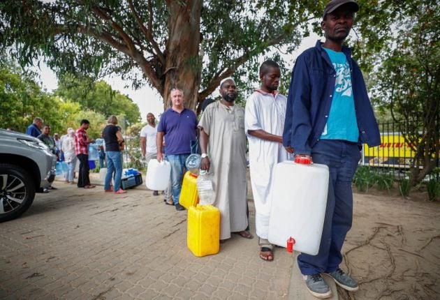 Varias personas hacen cola para llenar garrafas de agua procedente de un arroyo en un punto de recogida en Ciudad del Cabo (Sudáfrica).