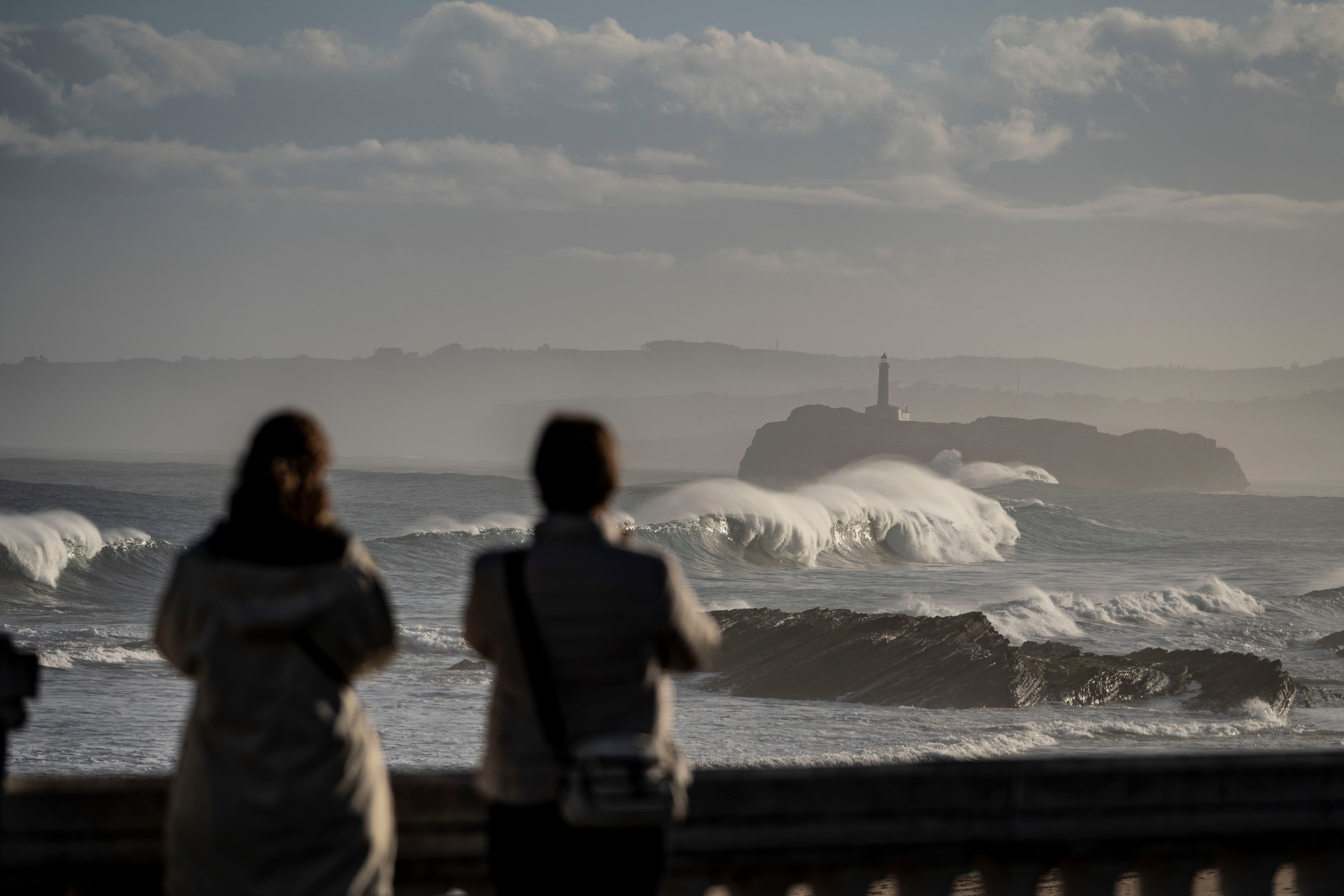 SANTANDER, 27/01/2025.-Dos mujeres hacencon la Isla de Mouro al fondo, en la bahía de Santander, este lunes. La borrasca Herminia que azota todo el país, mantiene la alerta naranja por fenómenos costeros en la costa desde las 9.00 a las 23.00 horas, y el nivel de riesgo es amarillo en la Cantabria del Ebro hasta las 18.00 horas por viento.-EFE/ Román G.aguilera
