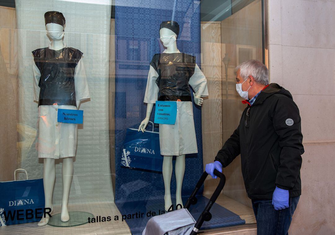 Un hombre protegido con mascarilla observa un escaparate de ropa.