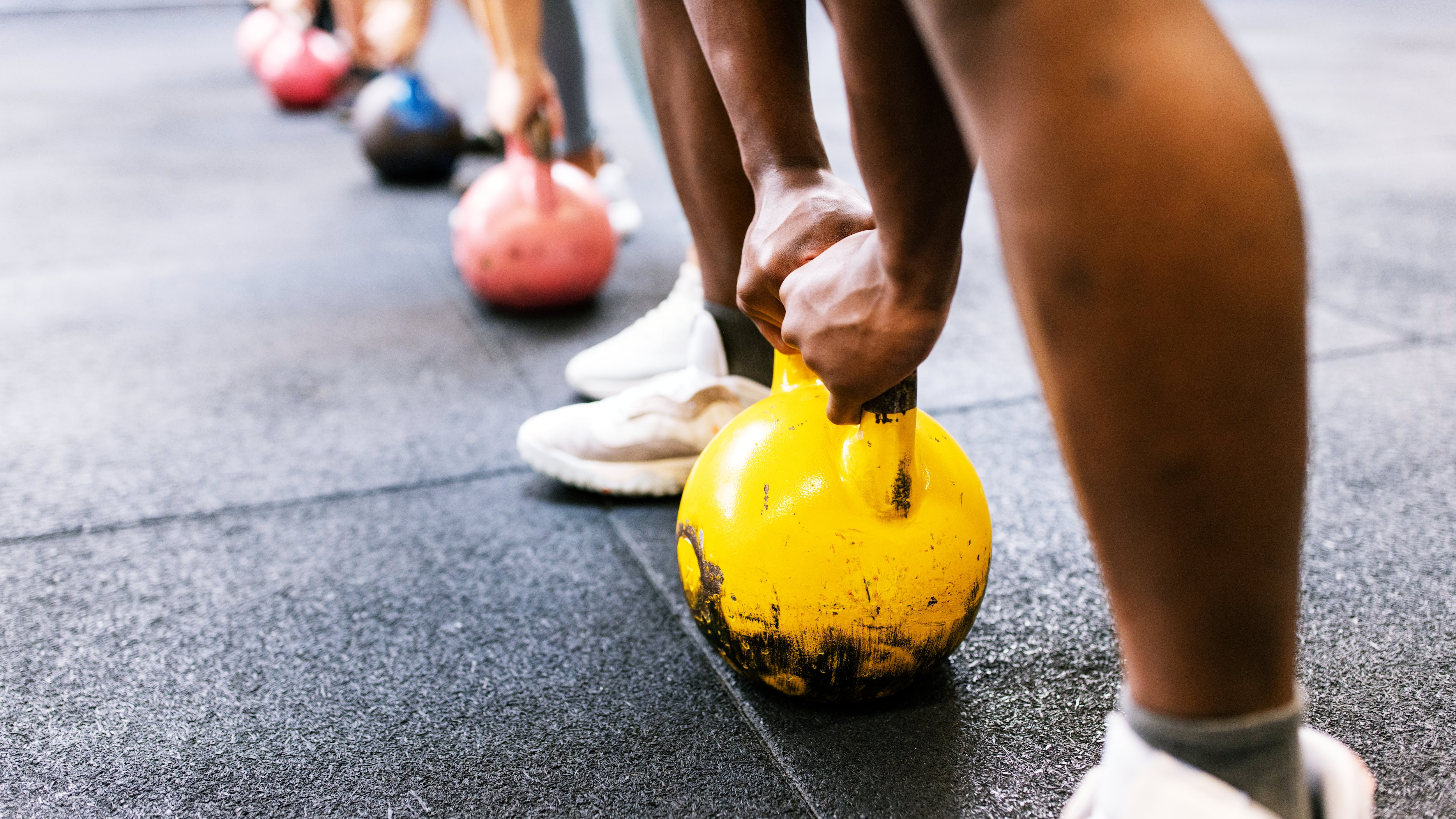 Closeup of people hands lifting kettle bell at gym. Athlete people in fitness center doing weight lifting with kettlebell at cross training gym.