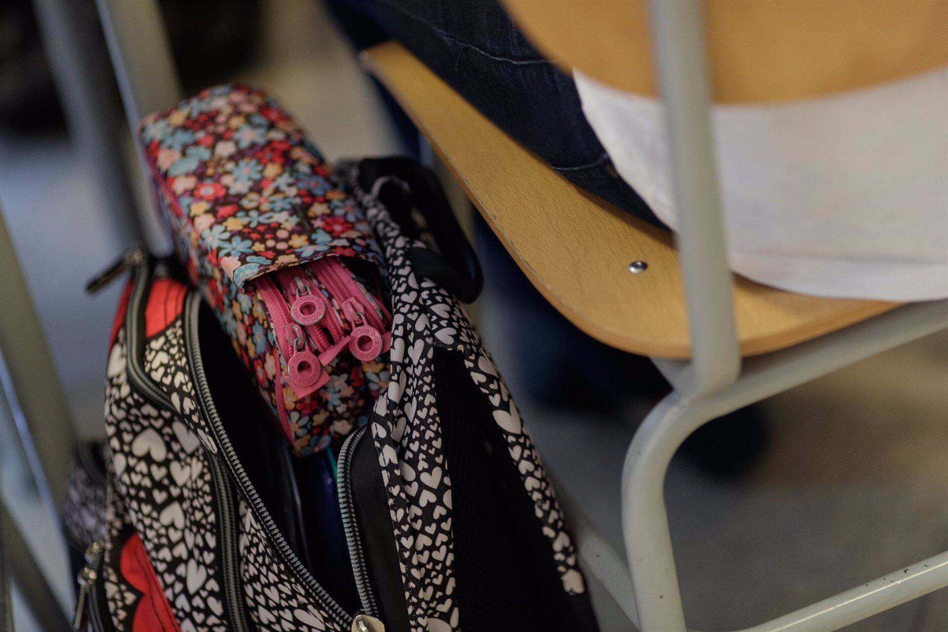 Mochila de un estudiante colgada de la silla junto a un pupitre