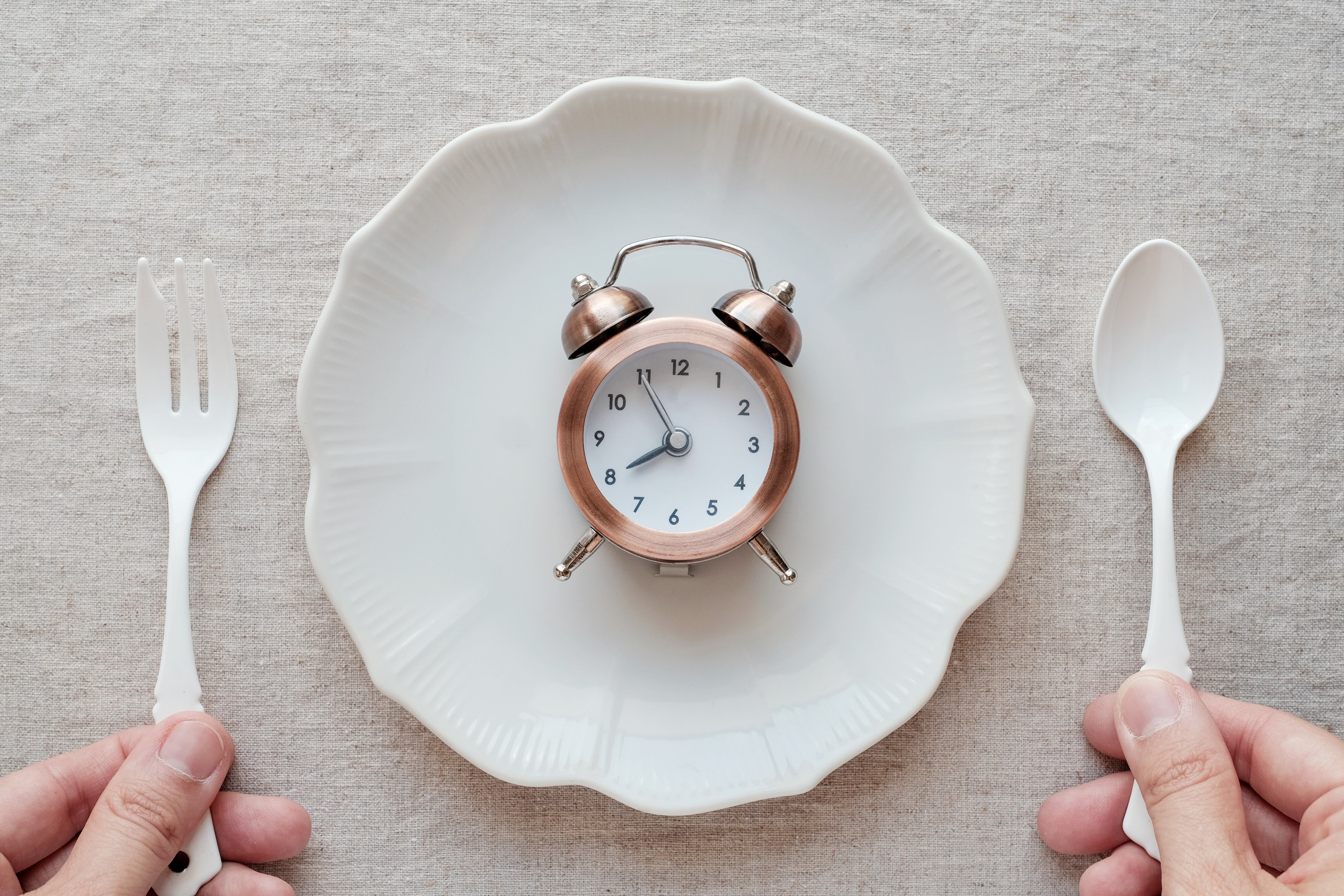 Unas manos sostienen un cuchillo y un tenedor frente a un plato con un reloj.