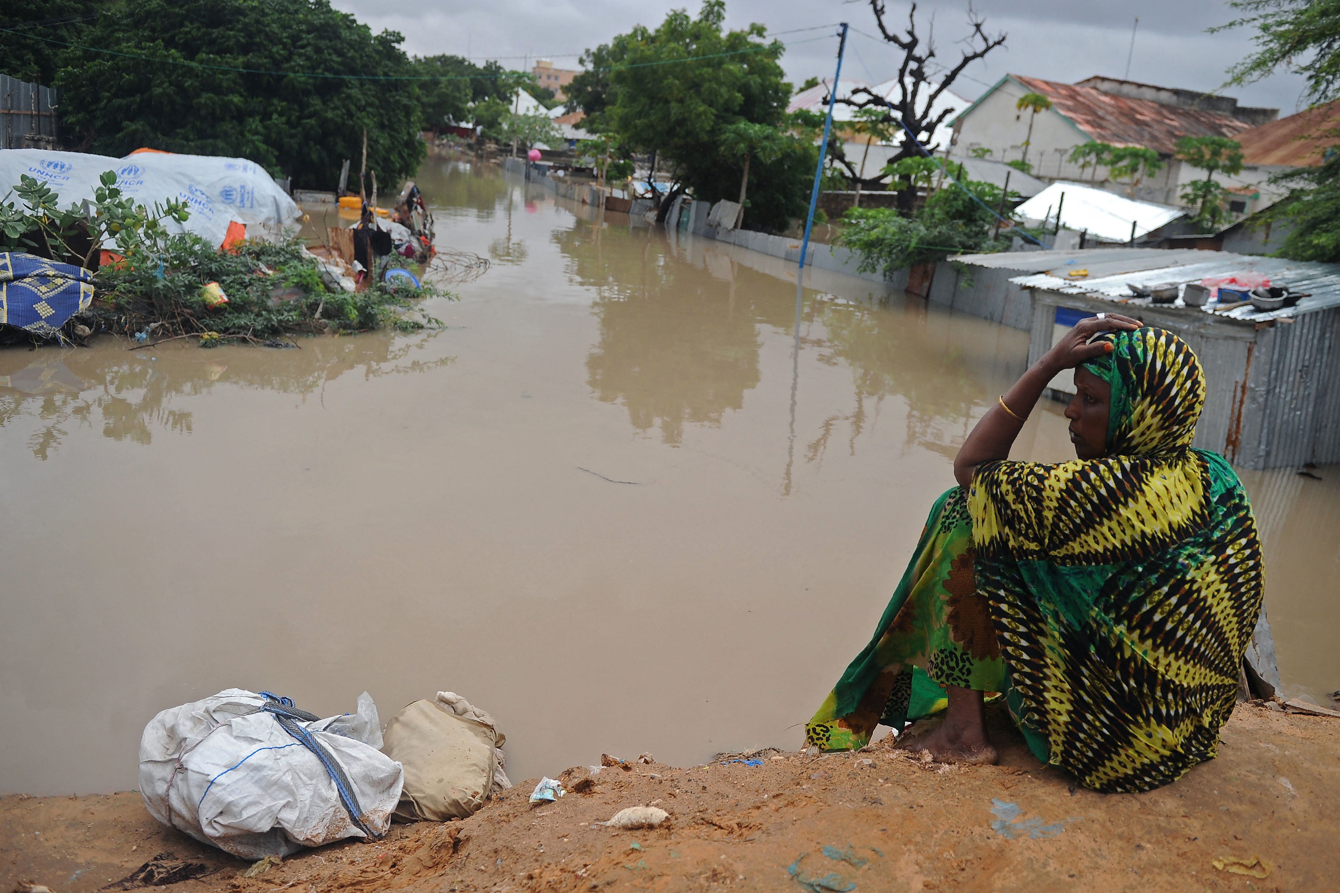 TOPSHOT - A woman living at a camp for the internally displaced sits on high ground above a flooded street on May 20, 2018 in Mogadishu after temporary shelters were inundated in Somalia&#039;s capital following heavy overnight rainfall. (Photo by MOHAMED ABDIWAHAB / AFP) (Photo by MOHAMED ABDIWAHAB/AFP via Getty Images)