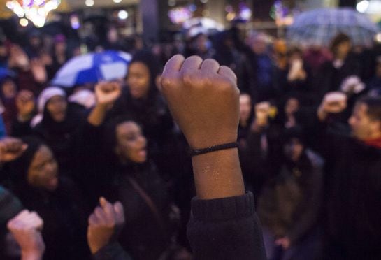 Personas con puños al aire y cantando durante una manifestación en contra de la decisión del gran jurado por el tiroteo Ferguson de Michael Brown, donde los manifestantes también interrumpieron los acontecimientos del Viernes Negro, en Seattle.