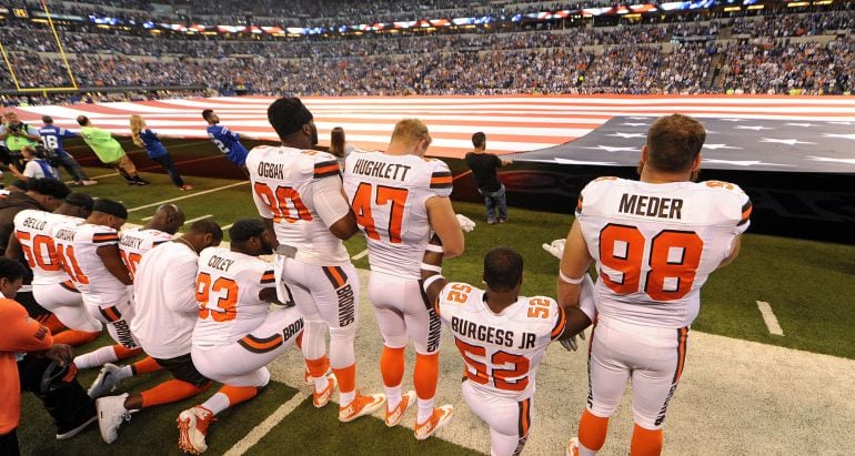 Algunos de los jugadores de los Cleveland Browns hincan la rodilla en el suelo mientras suena el himno de Estados Unidos.