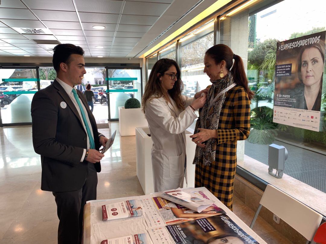Una doctora en la mesa informativa del Quirónsalud Sagrado Corazón explica a dos personas la importancia de la vacunación contra el VPH