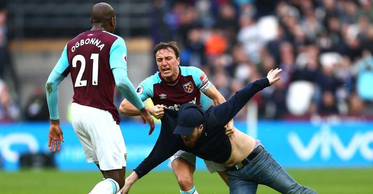 Mark Noble, capitán del West Ham, trata de echar a un Hooligan de su equipo que saltó tras el segundo gol del equipo visitante