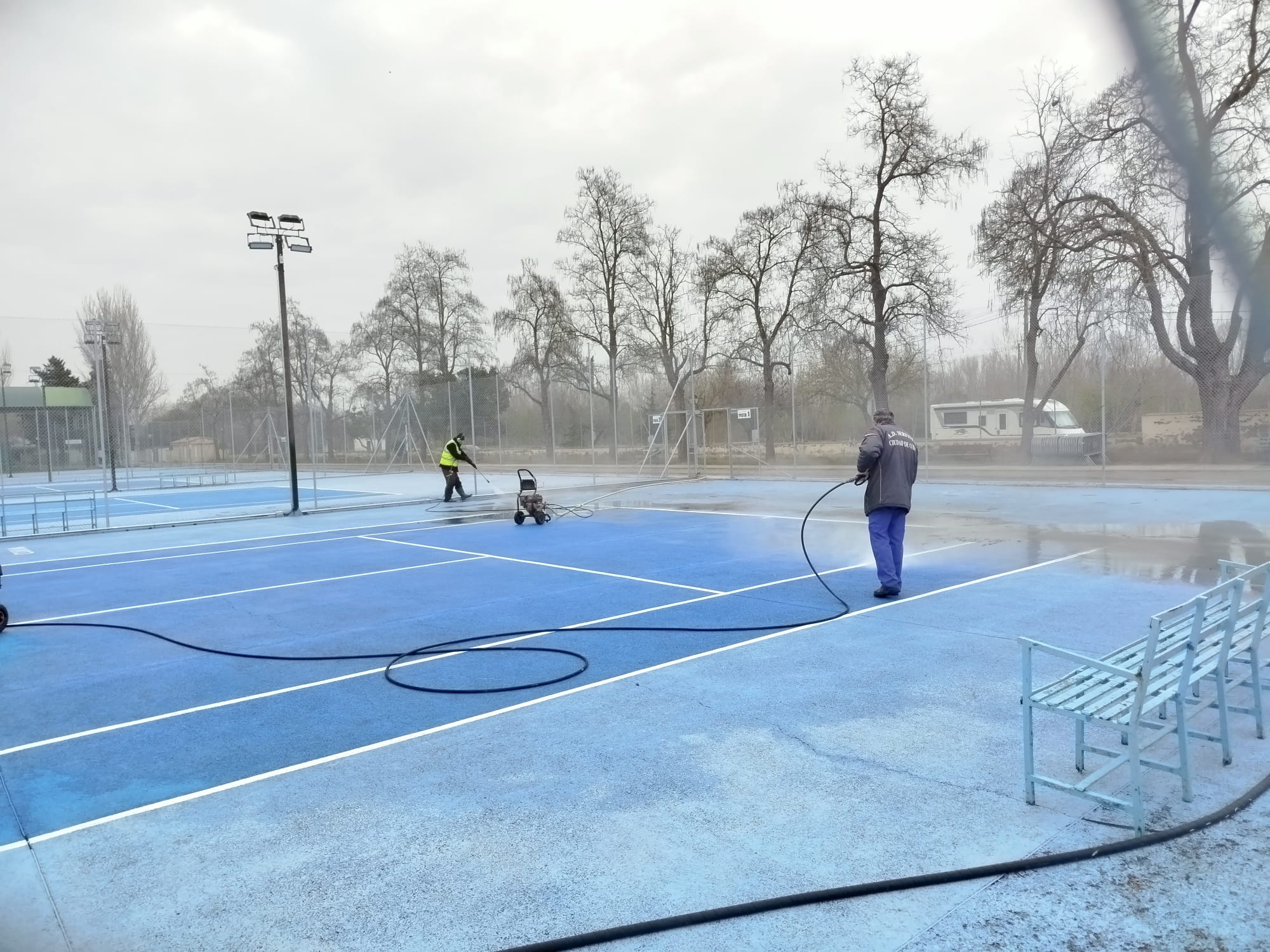 Operarios de limpieza trabajan en una cancha de tenis de Coria