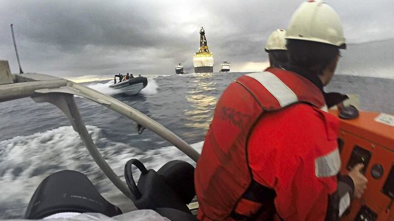 Fotografía facilitada por Greenpeace de dos activistas en una de sus lanchas y otra de la Armada española acercándose por la izquierda, durante la protesta frente a la plataforma Rowan Renaissance contra las prospecciones petrolíferas de Repsol en aguas d