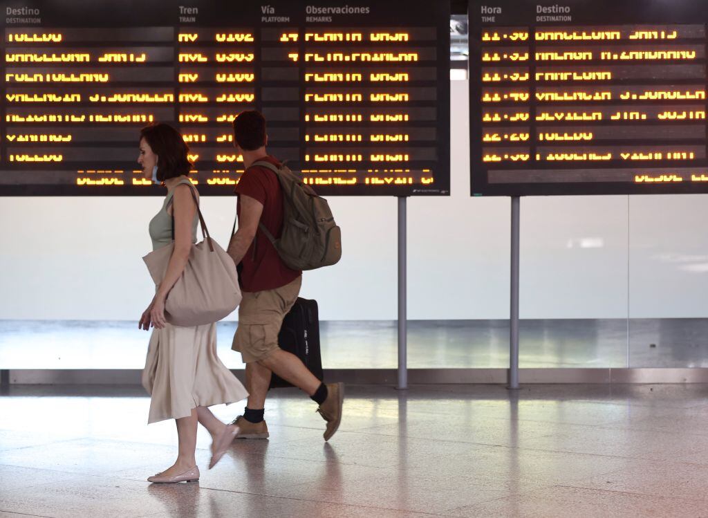 Pasajeros de Renfe pasan junto a una pantalla en Atocha, Madrid. Archivo.