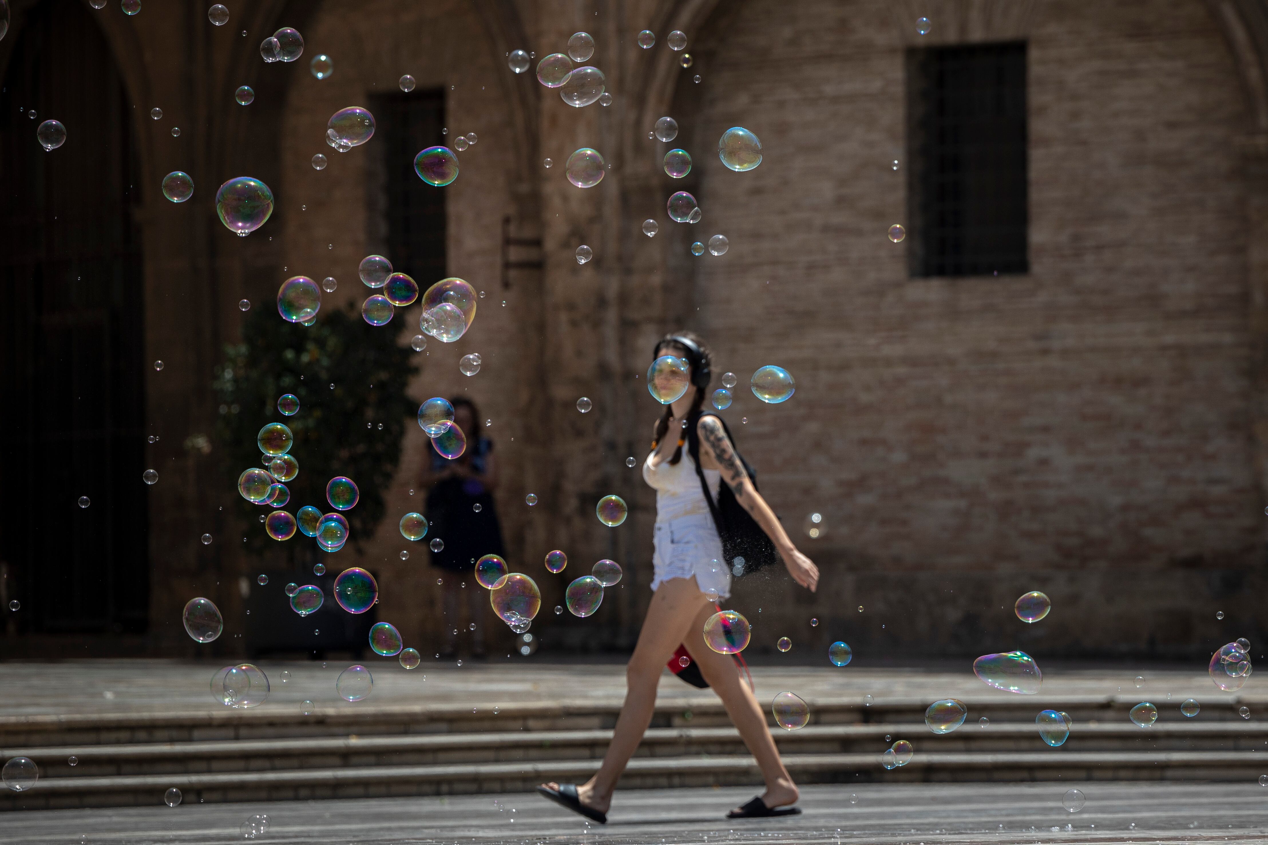 Una joven pasea entre pompas de jabón por la plaza de la Virgen de Valencia cuando el calor y el tiempo estival se mantienen durante estos primeros días del mes de julio