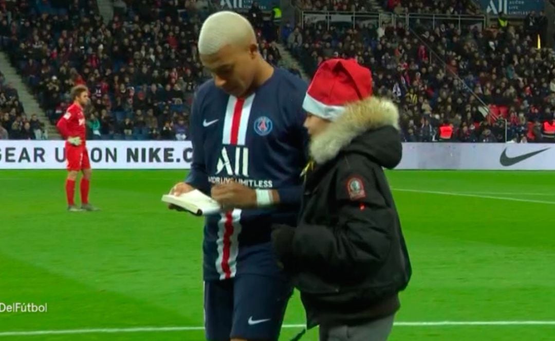 Mbappé firma un autógrafo mientras acompaña al niño fuera del campo