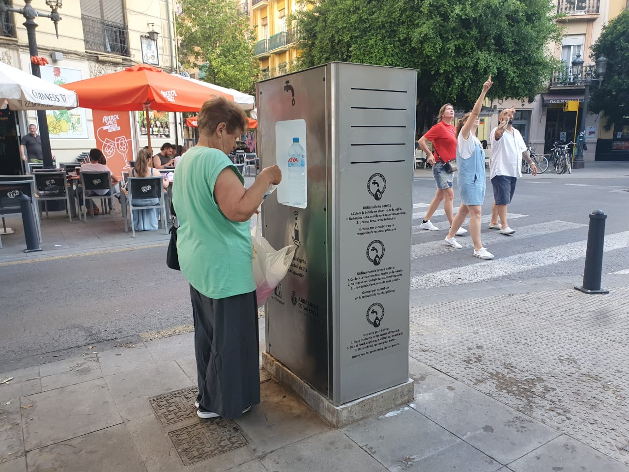 Una mujer rellena unas botellas de agua en una fuente municipal refrigerada.