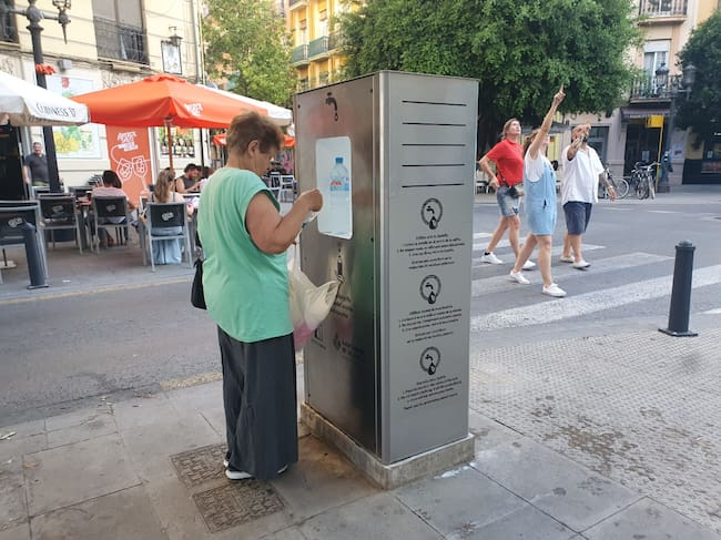 Una mujer rellena unas botellas de agua en una fuente municipal refrigerada.