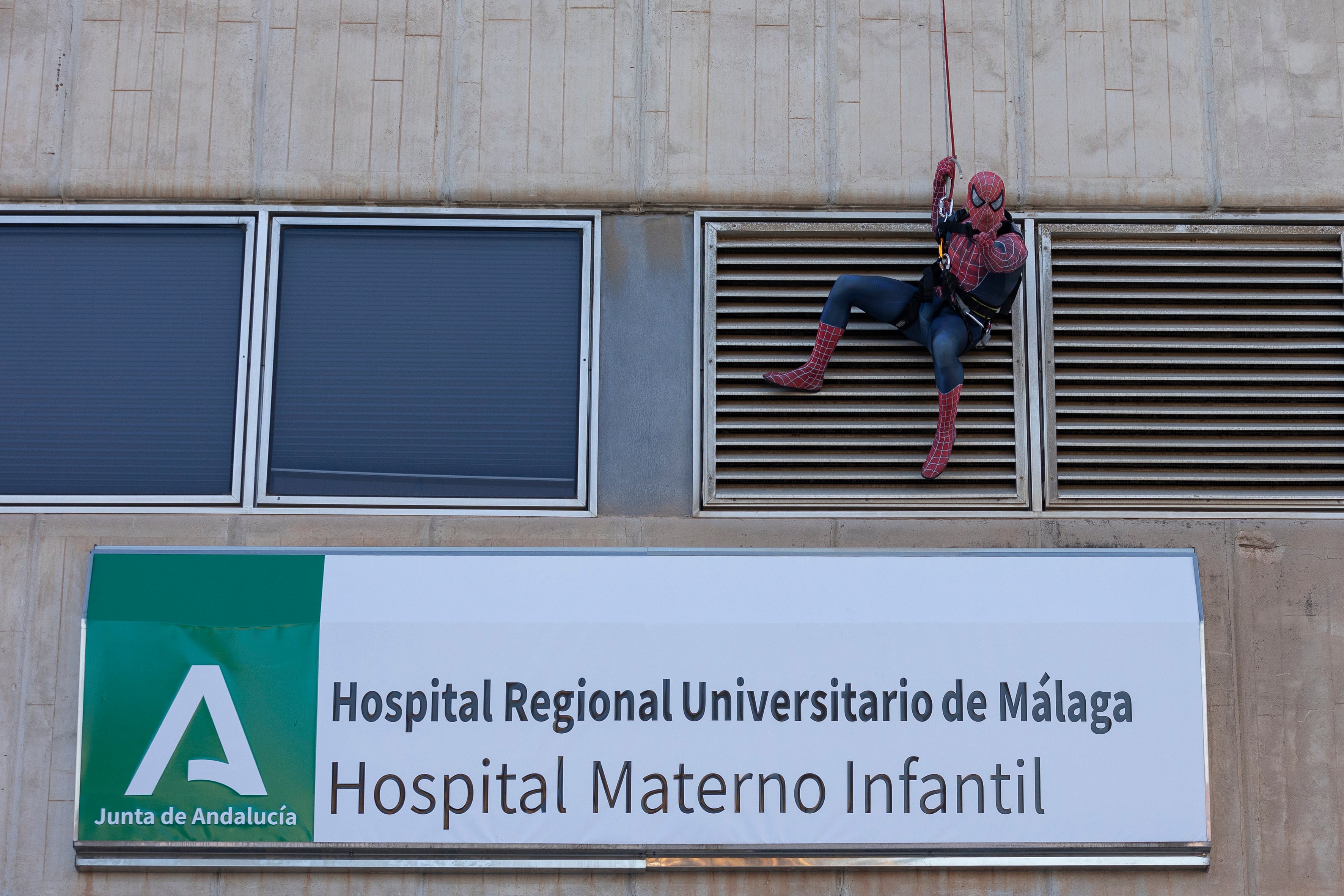 GRAFAND7553. MÁLAGA, 18/12/2023.- Spiderman se ha descolgado por la fachada del Hospital Materno de Málaga, desde el tejado con la ayuda de un bombero, para saludar a los niños ingresados en las plantas de enfermedades infecciosas, Oncología, Lactantes y Cirugía a través de las ventanas. EFE/Carlos Díaz
