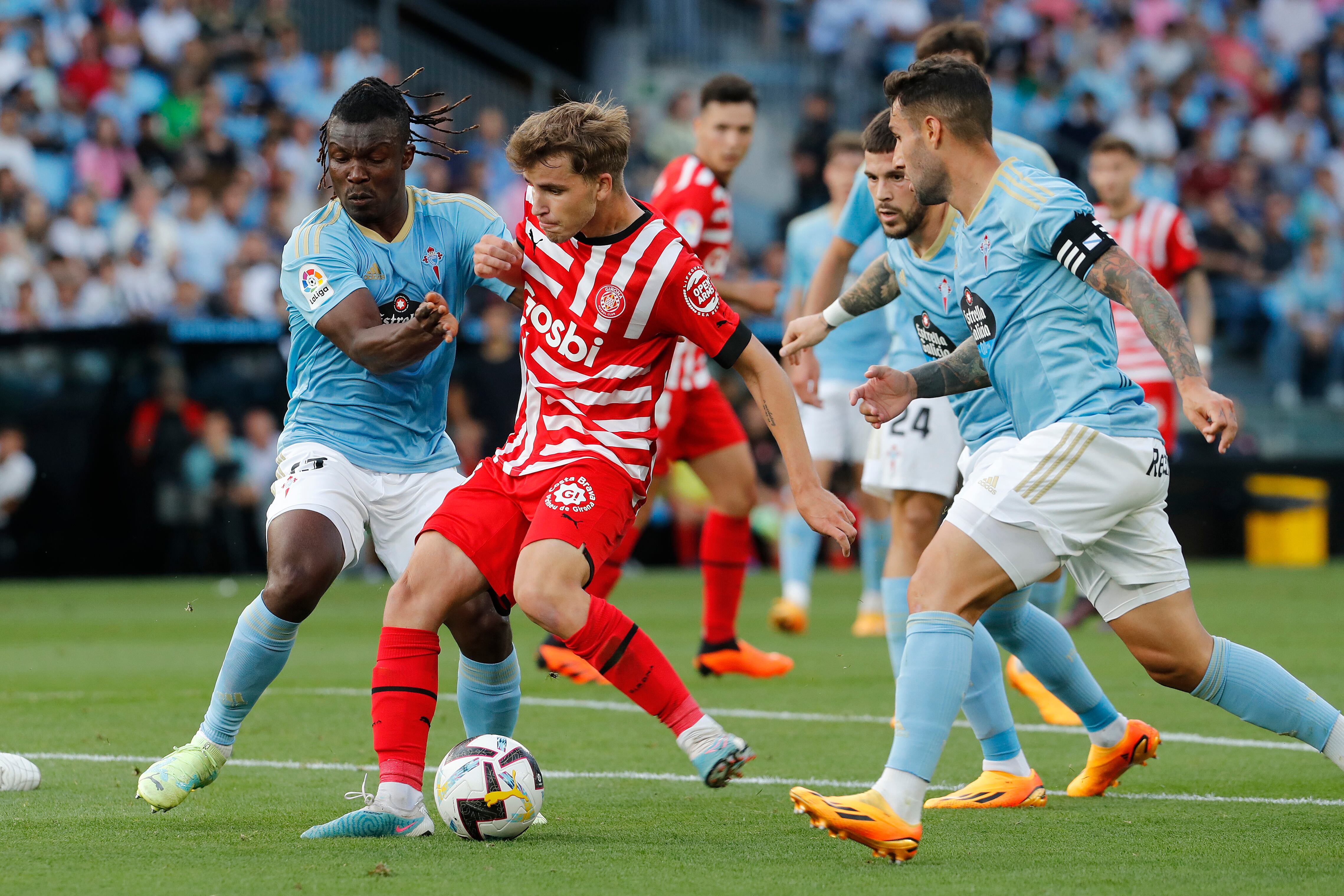 VIGO (PONTEVEDRA), 23/05/2023.- El centrocampista del Girona Ricard Artero (2-i) trata de jugar un balón ante Joseph Aidoo (i), del Celta, durante el partido de Liga en Primera División que Celta de Vigo y Girona FC disputan este martes en el estadio de Balaídos. EFE/Salvador Sas
