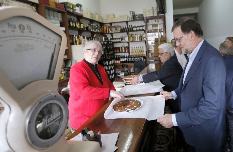 El presidente del Gobierno, Mariano Rajoy, recibe una tarta que le regala la dueña de una tienda en agradecimiento por su visita, durante paseo por Vilalba