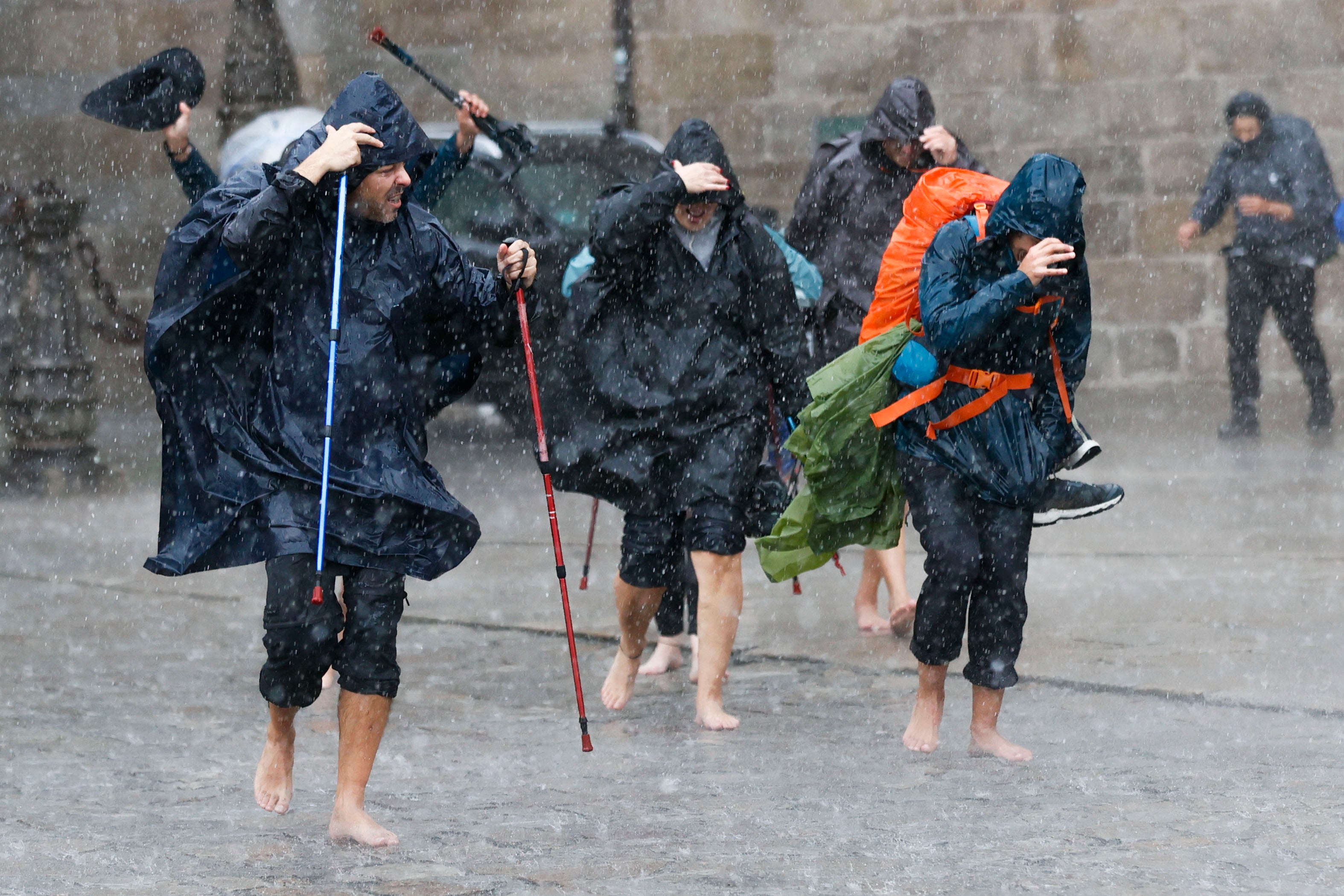 Un grupo de peregrinos termina el Camino de Santiago bajo un chubasco esta mañana en el plaza del Obradoiro, en Santiago de Compostela, que ha traído la nueva borrasca.