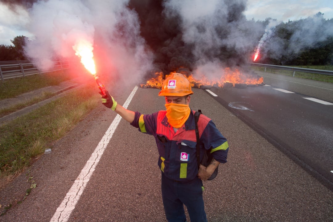 Un trabajador de Alcoa San Cibrao enciende una bengala durante una manifestación en la que han cortado la Autopista A6 con la quema de neumáticos, en Outeiro de Rei, Lugo.