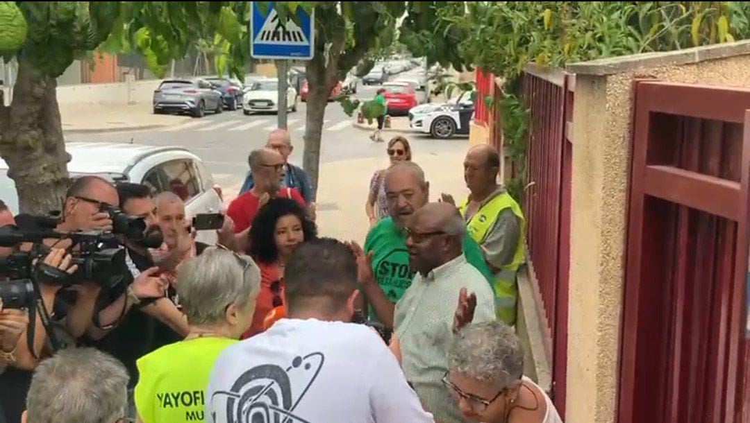 Donato Ndongo en el portal de su vivienda en el barrio murciano de Espinardo, arropado por colectivos sociales y vecinos, atiende a los medios de comunicación. Foto: IU-Verdes.