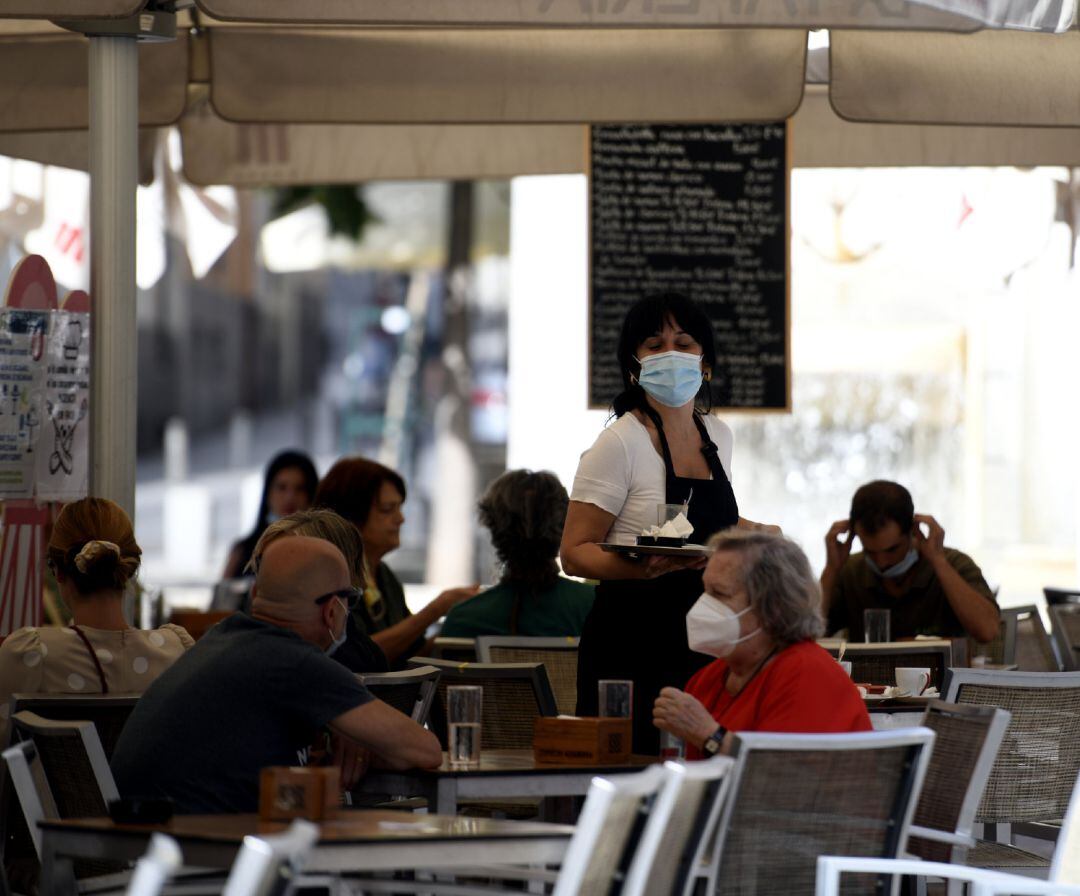 Una camarera con mascarilla atiende a los clientes en una terraza de un bar