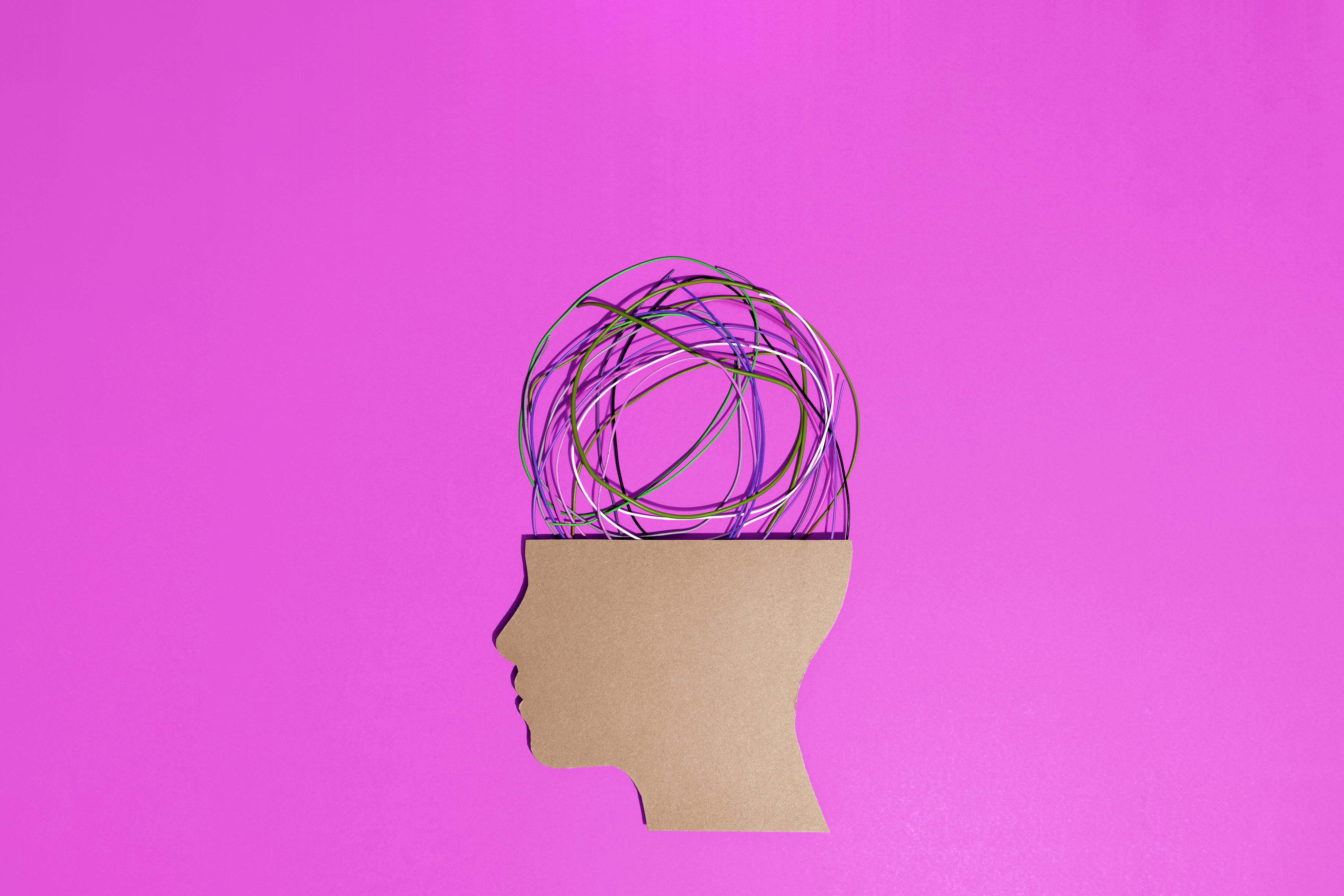 Conceptual image of a cardboard human head silhouette with tangled colorful wires coming out of it representing stress, anxiety and mental health