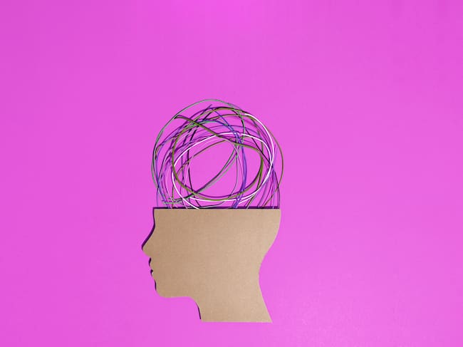 Conceptual image of a cardboard human head silhouette with tangled colorful wires coming out of it representing stress, anxiety and mental health