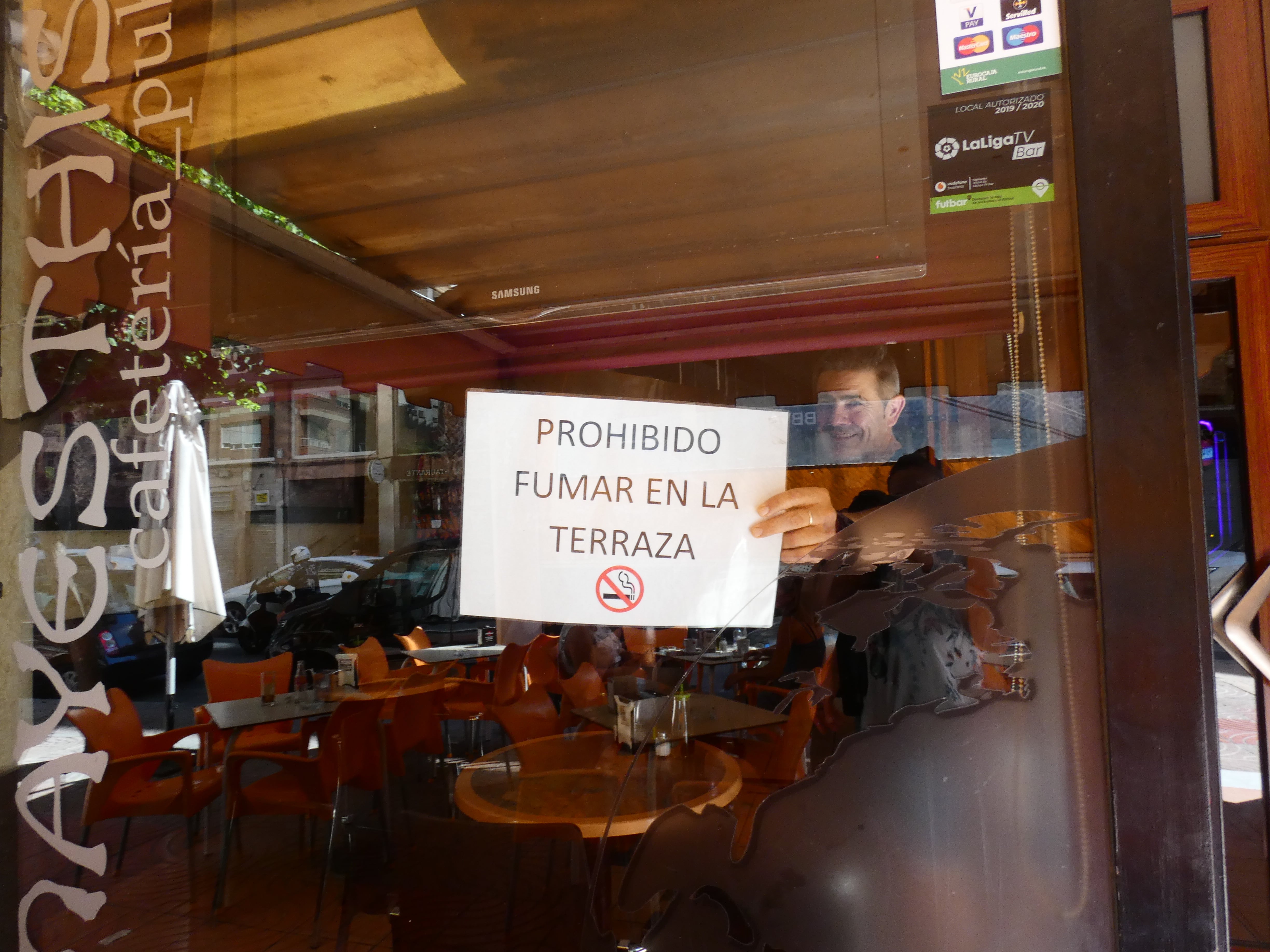 Hostelero muestra como quita el cartel de prohibido fumar en la terraza.