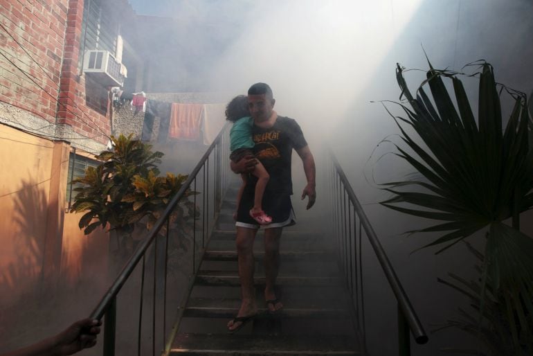 Un hombre camina desde su casa y con su hijo en brazos mientras los trabajadores fumigan la zon para terminar con los mosquitos que transmiten el virus Zika. 