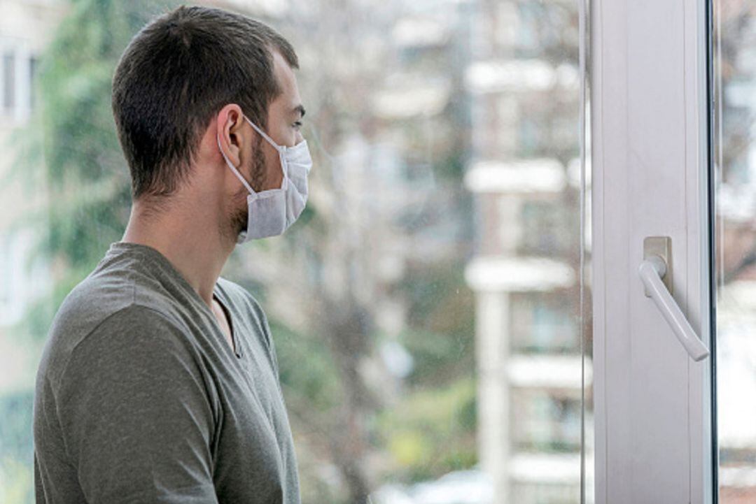 Hombre con mascarilla mirando a través de una ventana 