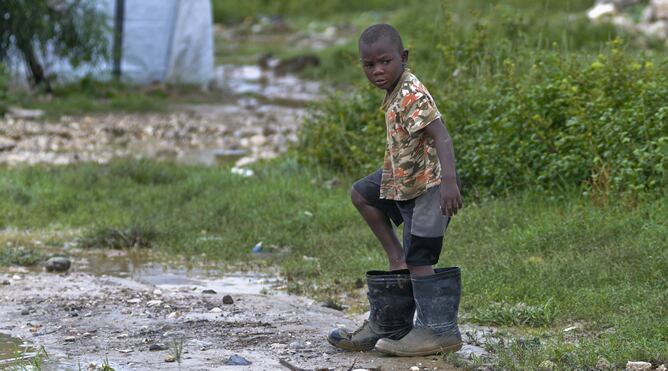 Un niño se pone unas grandes botas de agua tras el paso del huracán &#039;Sandy&#039; por Haití