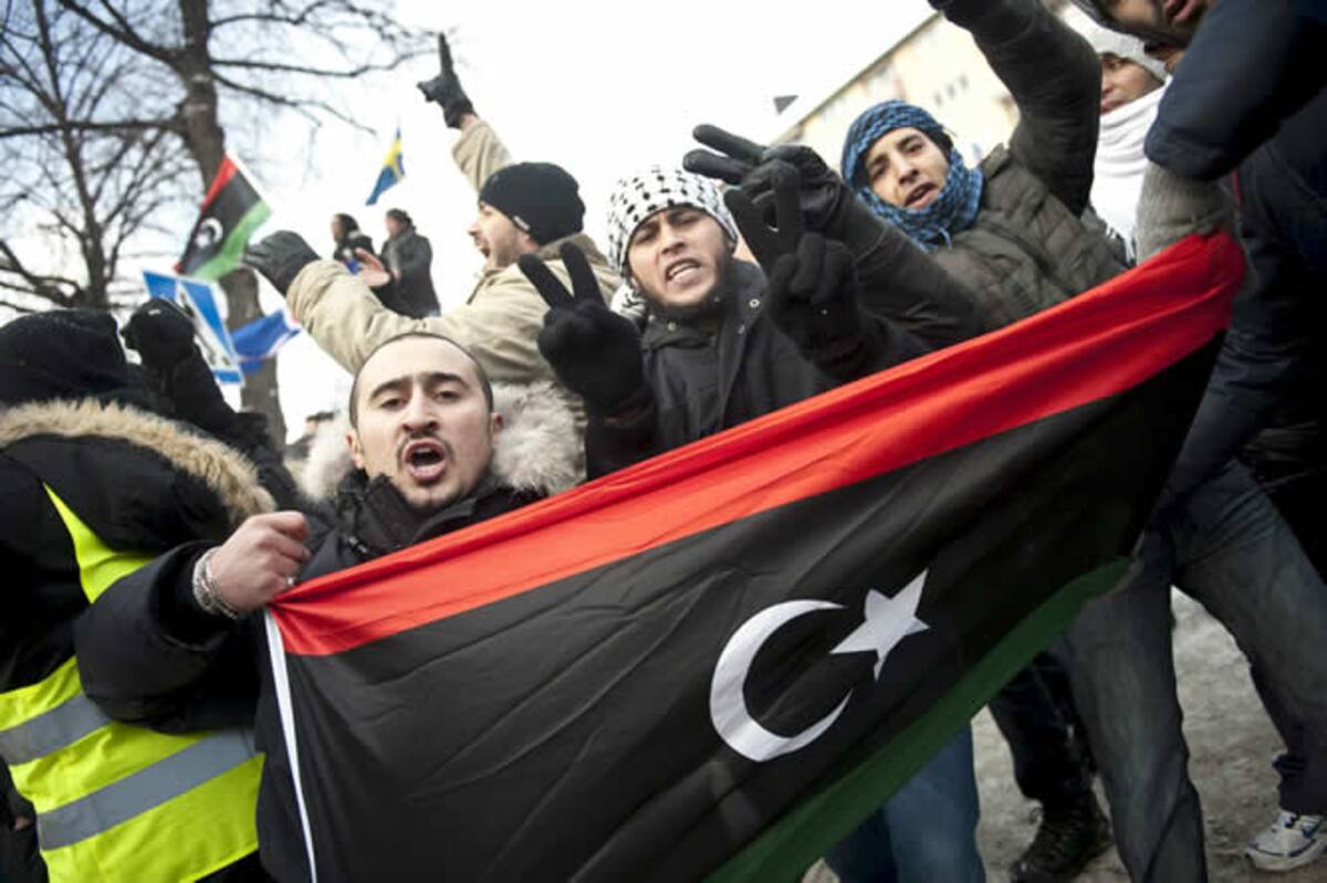 Manifestantes libios ondean la antigua bandera libia durante una protesta en contra del gobernante libio, Muamar el Gadafi, al frente de la embajada de Libia, en Estocolmo (Suecia)