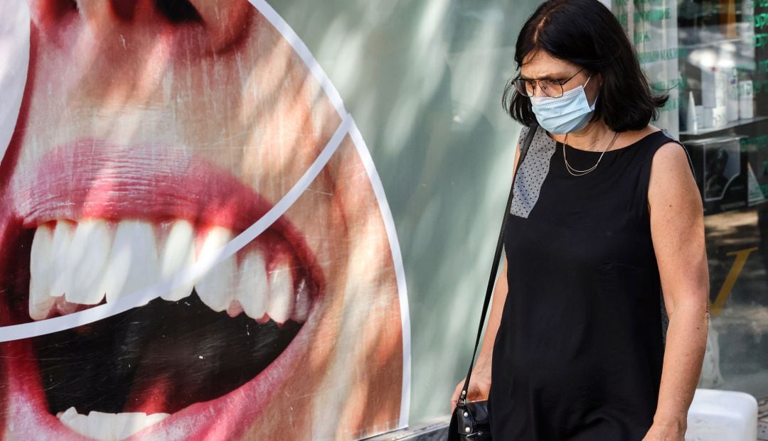 Una mujer con mascarilla pasea frente al escaparate de una clínica dental