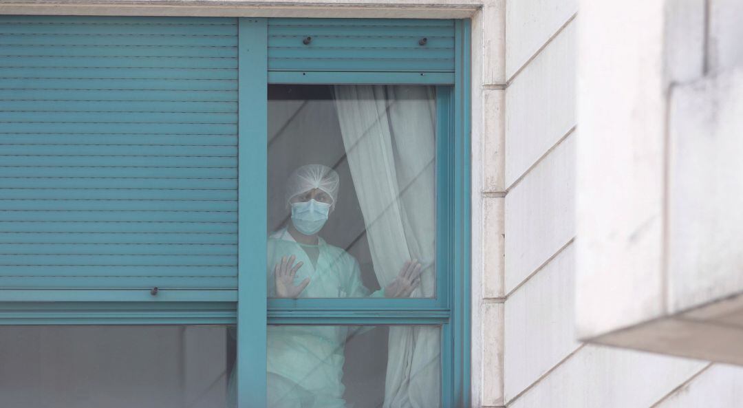 Archivo - Una trabajadora del personal sanitario protegida con mascarilla se asoma por una de las ventanas de una residencia.
